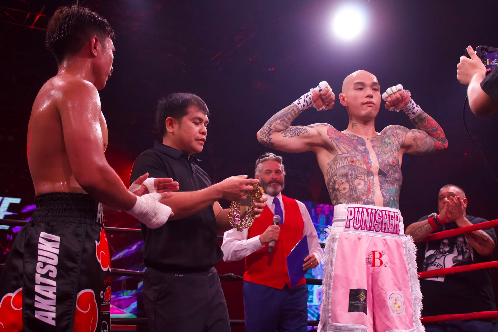 James Tang 'The Punisher' flexing in the ring after a win, wearing pink and white Primal boxing trunks.