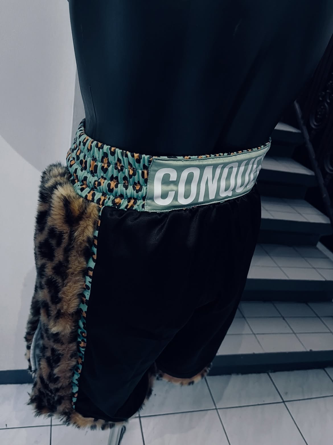 Black custom Aaron Clarke Muay Thai shorts with leopard trim, back view
