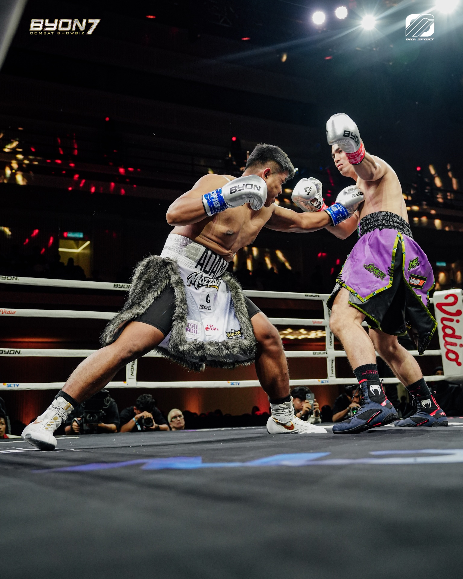 Adam Maulana in white boxing trunks with grey fur trim, mid-exchange during a bout.