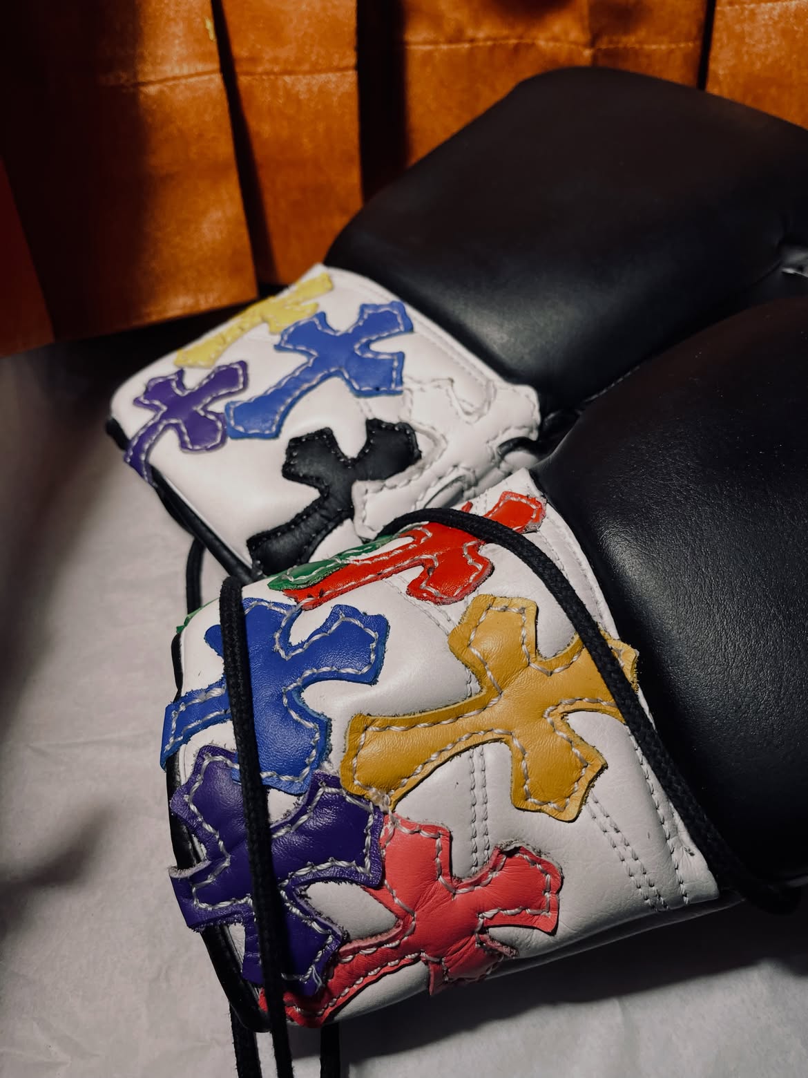 Custom Chrome Hearts inspired boxing gloves with multicoloured leather cross appliqué on a black leather couch.