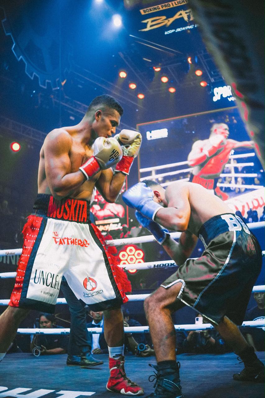 Maikhel Muskita in fighting stance wearing custom Primal trunks with his name on the waistband and boxing gloves raised.